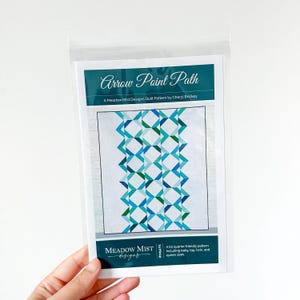 May include: A quilt pattern titled "Arrow Point Path" by Cheryl Brickey, featuring a geometric design in shades of blue and green. The pattern is packaged in a clear plastic sleeve. The Meadow Mist Designs logo is visible.