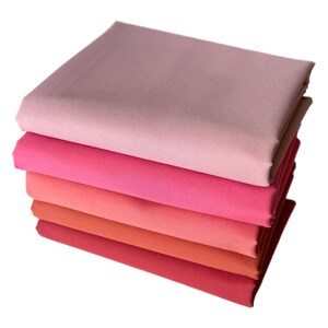 May include: A stack of six folded fabric squares in shades of pink and red. The colors range from light pink to deep red, creating a gradient effect. The fabric appears to be smooth and solid.