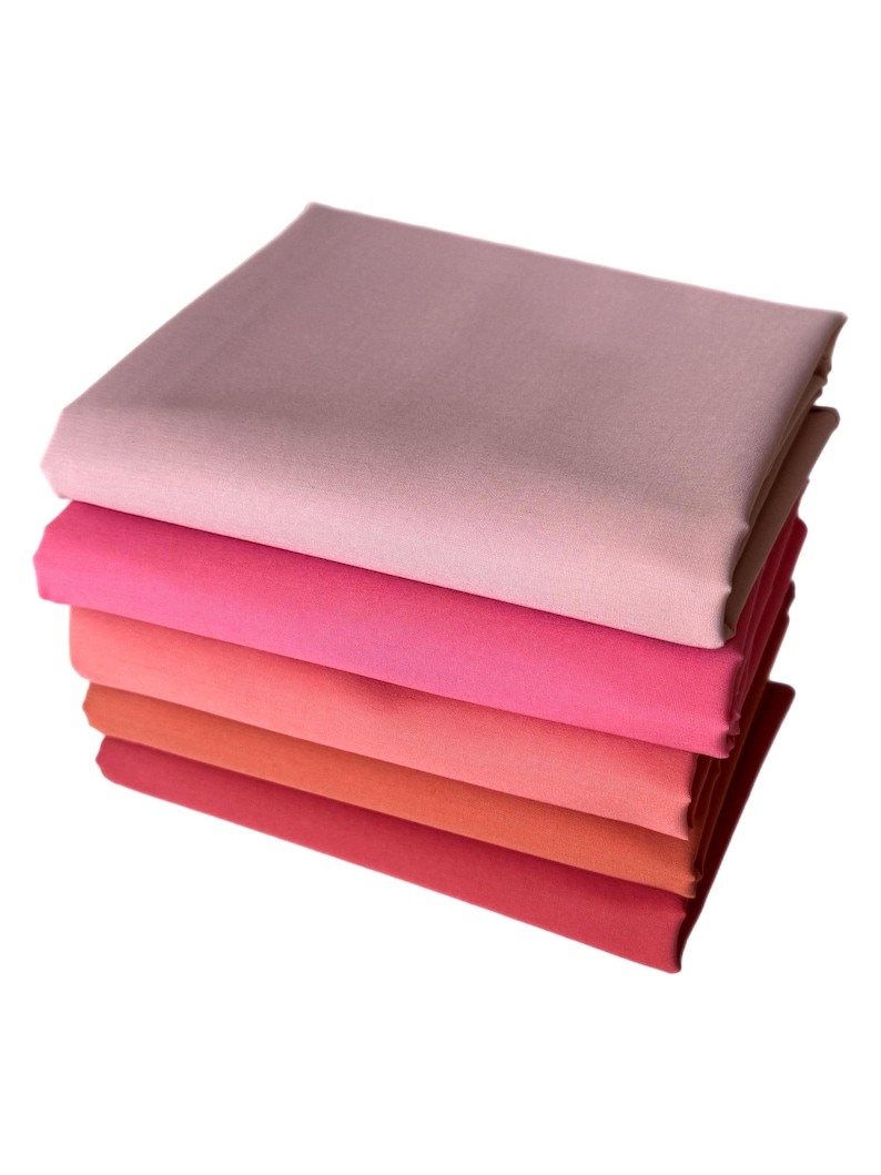 May include: A stack of six folded fabric squares in shades of pink and red. The colors range from light pink to deep red, creating a gradient effect. The fabric appears to be smooth and solid.