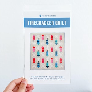 May include: A clear plastic package containing a quilt pattern. The pattern is titled "Firecracker Quilt" and features a design of colorful fireworks. The text "Standard Piecing Quilt Pattern for Beginner Level Sewers and Up" is also visible.