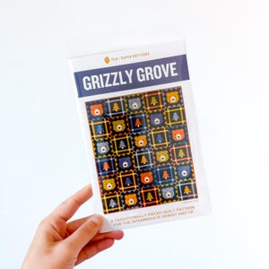 May include: A clear plastic package containing a quilt pattern titled "GRIZZLY GROVE." The pattern features a repeating design of colorful bear and tree motifs on a dark background. Text at the bottom reads "A TRADITIONALLY PIECED QUILT PATTERN FOR THE INTERMEDIATE SEWIST AND UP."