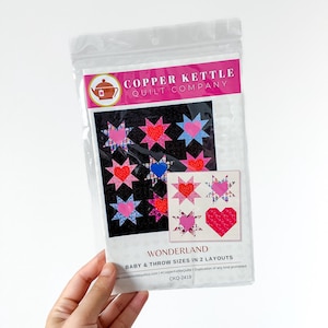 May include: A clear plastic package containing a quilt pattern. The pattern features a black background with star and heart designs in pink, red, and blue. The text "WONDERLAND" is visible.