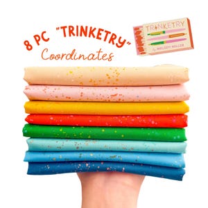 May include: A stack of eight fabric pieces in various colors, including yellow, pink, and blue, with gold speckles. The text "8 PC 'TRINKETRY' Coordinates" is displayed above the fabric. A small box with pen illustrations is also visible.