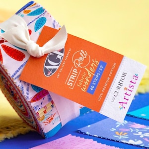 May include: A fabric strip roll tied with a cream ribbon. The roll features colorful patterned fabric with red, blue, and white designs. An orange tag reads "STRIP Roll wonders" and "40 STRIPS / 2.5"" with the brand name "Art Gallery Fabrics".