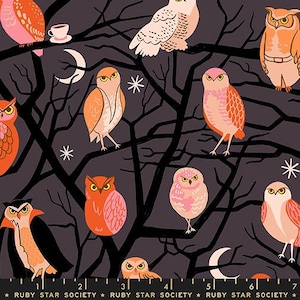 May include: A dark gray fabric featuring a repeating pattern of owls in shades of orange, pink, and cream perched on black tree branches. The design includes white crescent moons and star shapes, with a ruler showing 7 inches at the bottom.