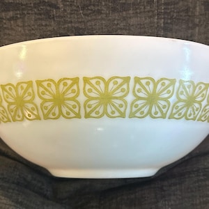 May include: White mixing bowl with a floral pattern in a light green color. The bowl has two handles and a rounded shape. The floral design is repeated around the bowl's exterior.