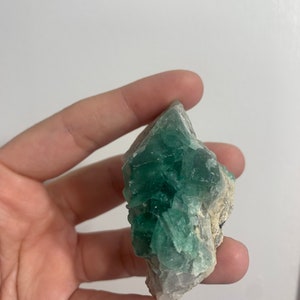 May include: A green fluorite crystal cluster with a rough, natural texture. The crystal is a light green colour and has a translucent appearance.