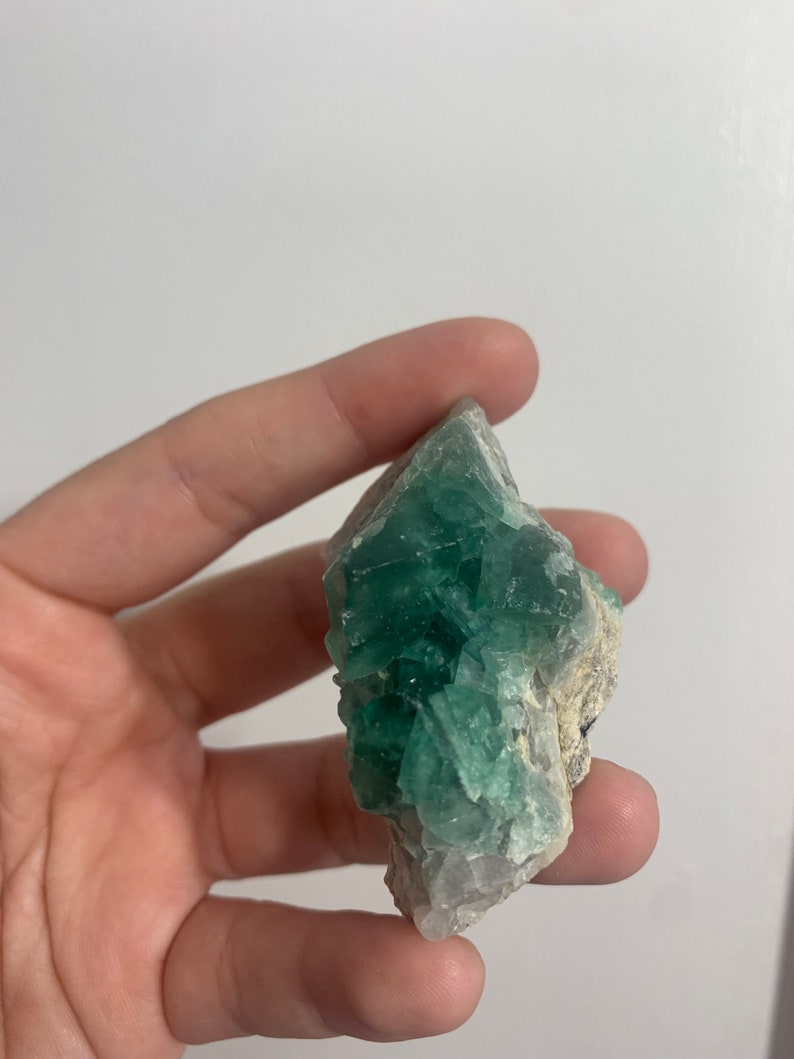 May include: A green fluorite crystal cluster with a rough, natural texture. The crystal is a light green colour and has a translucent appearance.