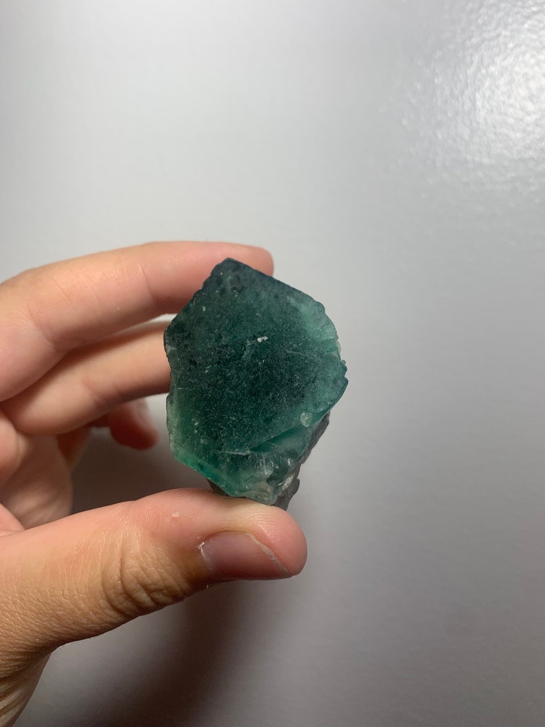 May include: A green fluorite crystal with a rough, natural texture. The crystal is translucent and has a slight shimmer.