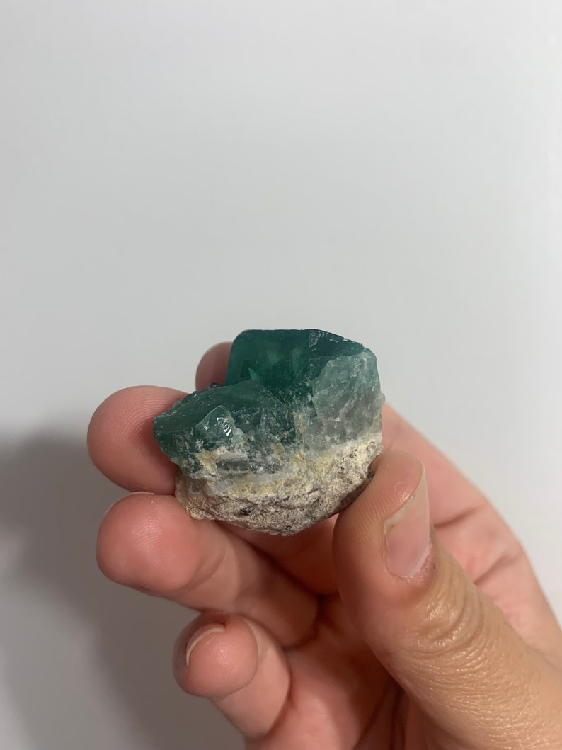 May include: A green fluorite crystal with a rough, natural texture. The crystal is a deep green colour and has a slightly cloudy appearance.