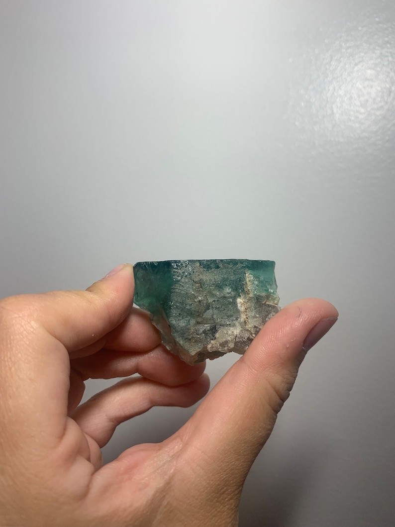 May include: A green fluorite crystal with white inclusions. The crystal is rough and has a natural, unpolished look.
