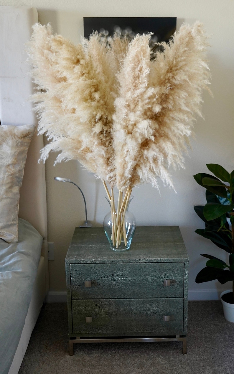 May include: A bouquet of dried pampas grass in a clear glass vase on a dark gray nightstand with two drawers. The nightstand has a textured surface and silver drawer pulls.