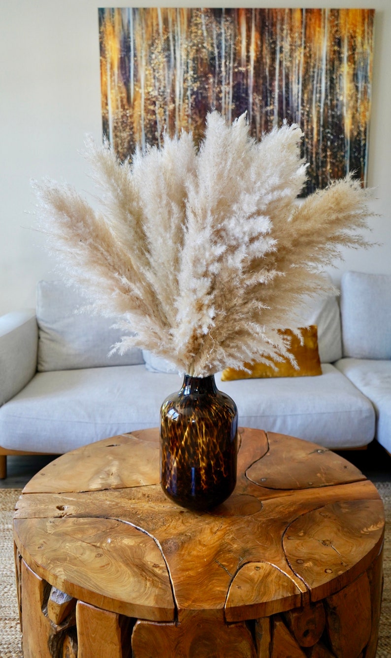 May include: A vase with a brown and black leopard print design filled with dried pampas grass sits on a wooden coffee table with a unique, irregular shape.