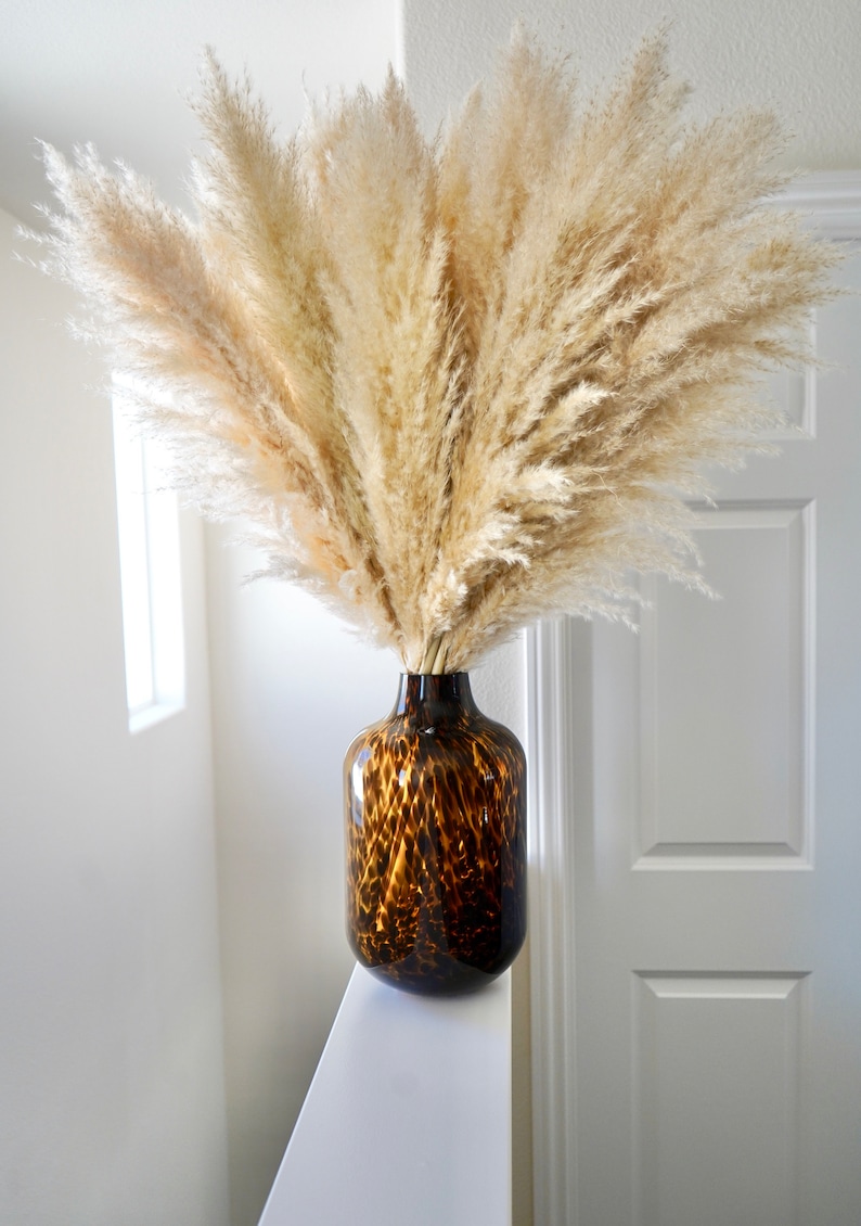 May include: A large bouquet of dried pampas grass in a brown and tan leopard print vase.