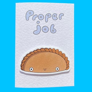 May include: A white card with the text "Proper Job" in blue letters. A cartoon pastry with a smiling face is on the card.