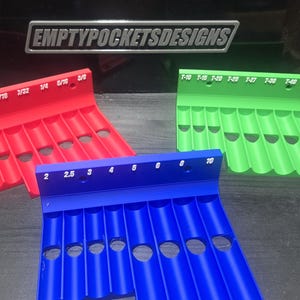 May include: Three plastic tool organizers in red, green, and blue, each featuring multiple slots and printed size labels. The red and green organizers have imperial measurements, while the blue one has metric labels. The text EMPTYPOCKETSDESIGNS is visible.