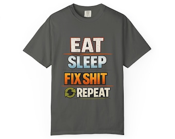 Puede incluir: Una camiseta de manga corta gris carbón con el texto EAT SLEEP FIX SHIT REPEAT en un diseño apilado y multicolor. Las palabras están impresas en una fuente desgastada con líneas horizontales que separan cada línea de texto y un icono.