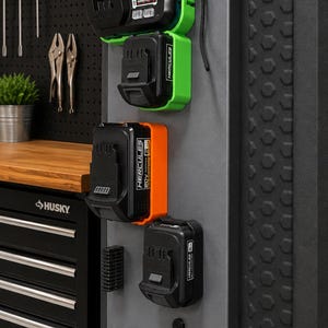 May include: A grey wall-mounted storage panel featuring a black and green Hercules 20V/12V lithium-ion battery charger, a black and green battery, a black and orange 20V battery, and a black battery, all organized with various black mounting brackets.