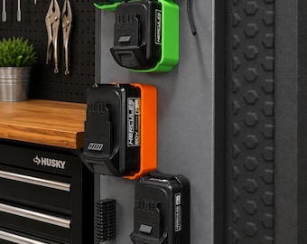 Puede incluir: Un panel de almacenamiento de pared gris que presenta un cargador de batería de iones de litio Hercules 20V/12V negro y verde, una batería negra y verde, una batería 20V negra y naranja, y una batería negra, organizadas con soportes negros.