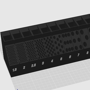 May include: A black rectangular organizer with nine vertical slots, each featuring a grid of circular holes of varying diameters. The front face displays printed numerical labels ranging from 1.5 to 9, corresponding to the size of the holes.