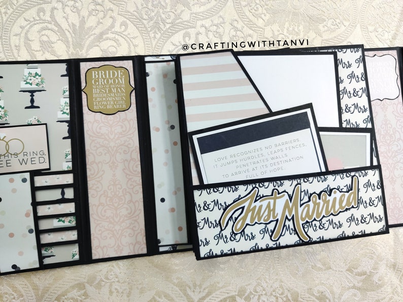May include: A black and white wedding scrapbook with a pink and white patterned background. The scrapbook is open to reveal a pocket with a quote about love and a card that says "Just Married".