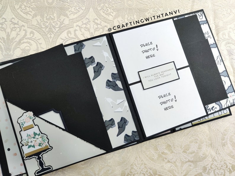 May include: A black scrapbook with white pages and a white card that says "Place Photo! Here" and "I will always remember the way you look tonight". The scrapbook has a white and gray patterned paper with images of shoes and a white cake with flowers.