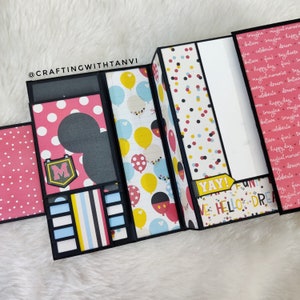 May include: A black and white scrapbook with a Mickey Mouse theme. The scrapbook is decorated with pink and white polka dots, yellow and blue balloons, and Mickey Mouse heads. The scrapbook is open to reveal a page with the words "YAY!" and "HELLO DREAM".