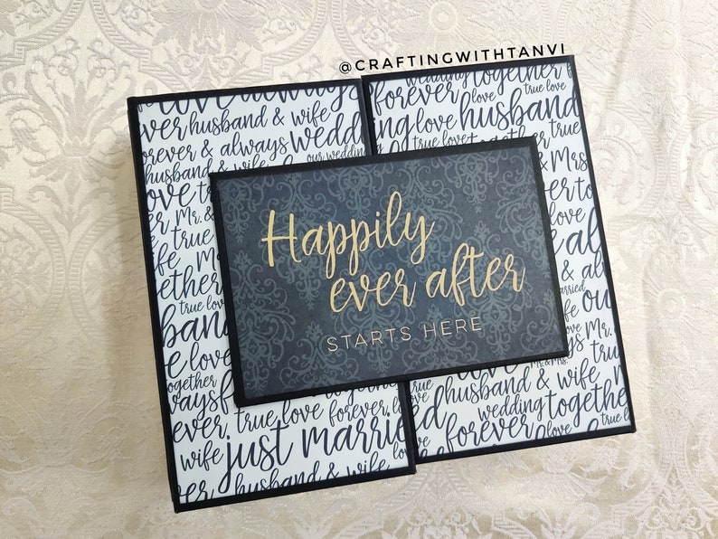 May include: A black framed sign with a gray background and gold lettering that reads "Happily ever after starts here". The background is a patterned design. The sign is surrounded by other black framed signs with white backgrounds and black lettering.