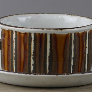 Könnte beinhalten: Eine weiße Suppenschüssel aus Keramik mit braunem und weißem Streifenmuster und zwei Henkeln. Die Schüssel steht auf einer passenden Untertasse.