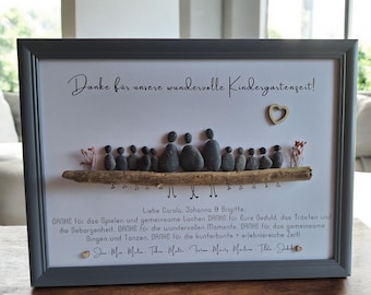 May include: A framed print with a hand-crafted pebble art design of a group of children sitting on a branch. The print has a white background and a gray frame. The text "Danke für unsere wundervolle Kindergartenzeit!" is written in black at the top of the print. The text "Liebe Carola, Johanna & Brigitte. DANKE für das Spielen und gemeinsame Lachen DANKE für Eure Geduld, das Trösten und die Geborgenheit. DANKE für die wundervollen Momente. DANKE für das gemeinsame Singen und Tanzen, DANKE für die kunterbunte erlebnisreiche Zeit!" is written in black at the bottom of the print.