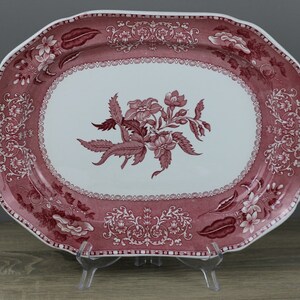 Könnte beinhalten: Eine weiße ovale Servierplatte mit einem rosafarbenen Blumendesign. Die Platte hat einen gewellten Rand und einen erhöhten Rand.