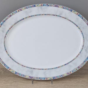 Könnte beinhalten: Eine ovale Servierplatte mit weißer Mitte, einem hellgrau marmorierten Rand und einem äußeren Bereich, der mit einem bunten, wirbelnden Muster in Blau-, Gelb-, Rosa- und Violetttönen verziert ist. Die Platte hat eine glatte, glänzende Oberfläche.