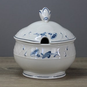 Könnte beinhalten: Weiße Zuckerdose aus Keramik mit blauem Blumendesign und einem Deckel mit Knauf. Die Schale hat eine runde Form und einen kleinen Ausguss am Deckel.