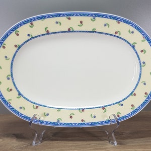 Könnte beinhalten: Ovale Servierplatte mit cremefarbenem Rand, verziert mit kleinen roten, blauen und grünen Blumenmustern. Der Rand wird von einem blauen geometrischen Design und einem weißen Rand umrahmt. Die Mitte ist schlicht weiß.