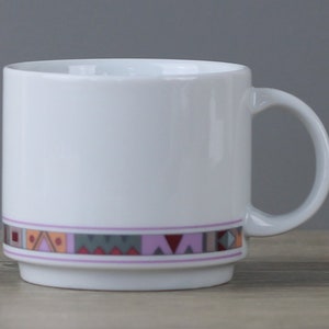 Könnte beinhalten: Weiße Keramiktasse mit einem geometrischen Muster in Rosa-, Orange- und Grautönen um den Rand.