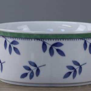 May include: White ceramic bowl with a green border and blue leaf pattern. The bowl has a cylindrical shape and a simple, elegant design. The leaves are arranged in a repeating pattern around the bowl's exterior.