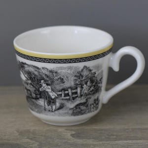 Könnte beinhalten: Eine weiße Keramiktasse mit einer schwarz-weißen pastoralen Szene, die eine Person an einem Zaun mit einem Hund zeigt. Der Rand ist mit einem dünnen gelben Band und einem schwarzen geometrischen Mäander-Muster verziert. Mit Henkel.