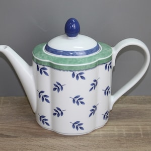 Op de afbeelding: Een witte theepot met een blauw en groen bloemenpatroon. De theepot heeft een deksel met een blauwe knop en een tuit aan de zijkant.