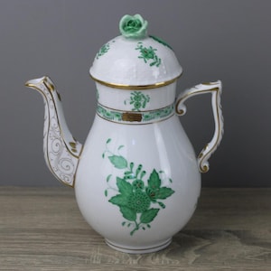 Puede incluir: Cafetera de porcelana blanca con diseños florales verdes y ribetes dorados. La tapa está rematada con una rosa verde. El asa y el pico también están adornados con oro. Una pieza decorativa para servir café o té.