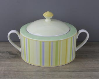 May include: A white ceramic sugar bowl with a lid. The bowl has a striped pattern in yellow, green, and purple. The lid has a yellow knob.