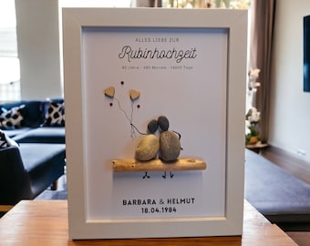 May include: A white framed picture with a white background. The picture features a couple made of stones sitting on a piece of driftwood. The couple is holding red heart balloons. The text "ALLES LIEBE ZUR Rubinhochzeit 40 Jahre - 480 Monate - 14600 Tage BARBARA & HELMUT 18.04.1984" is printed on the picture.