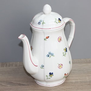 Puede incluir: Cafetera de cerámica blanca con un patrón floral en tonos de azul, amarillo, rojo y rosa. La cafetera tiene una tapa y un asa.