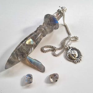 Könnte beinhalten: Ein graues Labradorit-Kristallpendel mit einer silbernen Kette und einem Sonnen- und Mond-Anhänger. Drei kleinere Labradorit-Kristalle sind ebenfalls abgebildet.