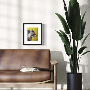 May include: A framed print of a raccoon with a yellow background. The raccoon is looking to the right of the frame. The frame is black and has a white mat.