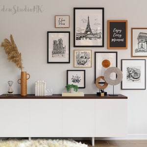 May include: A white cabinet with three doors sits on a dark wood surface. Above the cabinet is a gallery wall with black and white drawings of Paris landmarks, including the Eiffel Tower, Notre Dame Cathedral, and the Arc de Triomphe. The wall also features a wooden sign that says "Enjoy Every Moment".