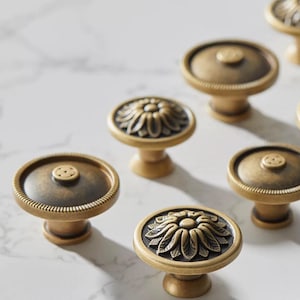 May include: A set of six antique brass cabinet knobs with a floral design. The knobs have a round base and a raised floral design in the centre.