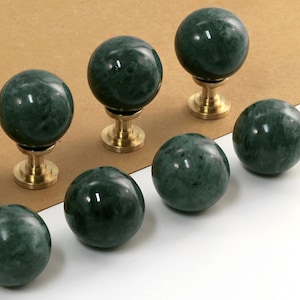 Può includere: Otto pomelli per armadi in marmo verde con basi in metallo dorato. I pomelli sono rotondi e hanno un motivo a spirale.
