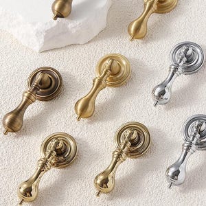 Puede incluir: Surtido de pomos para armarios en varios acabados, incluyendo latón, oro y plata. Los pomos tienen una base redonda y un mango en forma de lágrima.