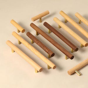 Puede incluir: Surtido de pomos y tiradores de cajones de madera con detalles en latón. Los pomos son de varios tamaños y formas, incluyendo redondos, cuadrados y rectangulares. Los tiradores son todos rectangulares y tienen un diseño simple y minimalista.