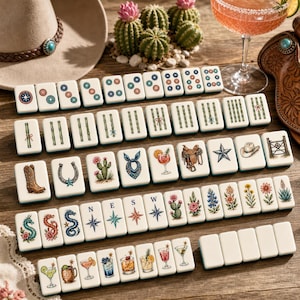 May include: A set of white mahjong tiles featuring colorful illustrations of western-themed icons, including cowboy boots, horseshoes, cacti, cocktails, dragons, and compass directions, arranged in rows on a wooden surface.